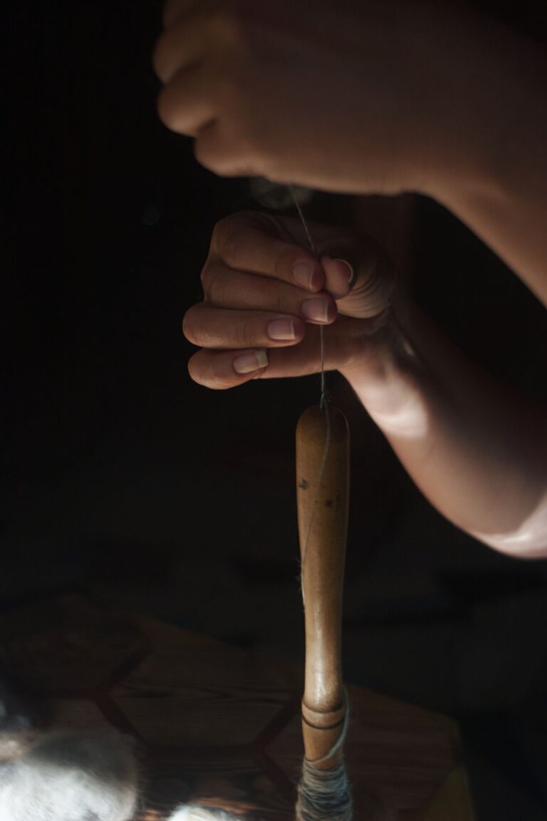 A focused close-up of hand spinning wool with a drop spindle, evoking traditional craftsmanship.