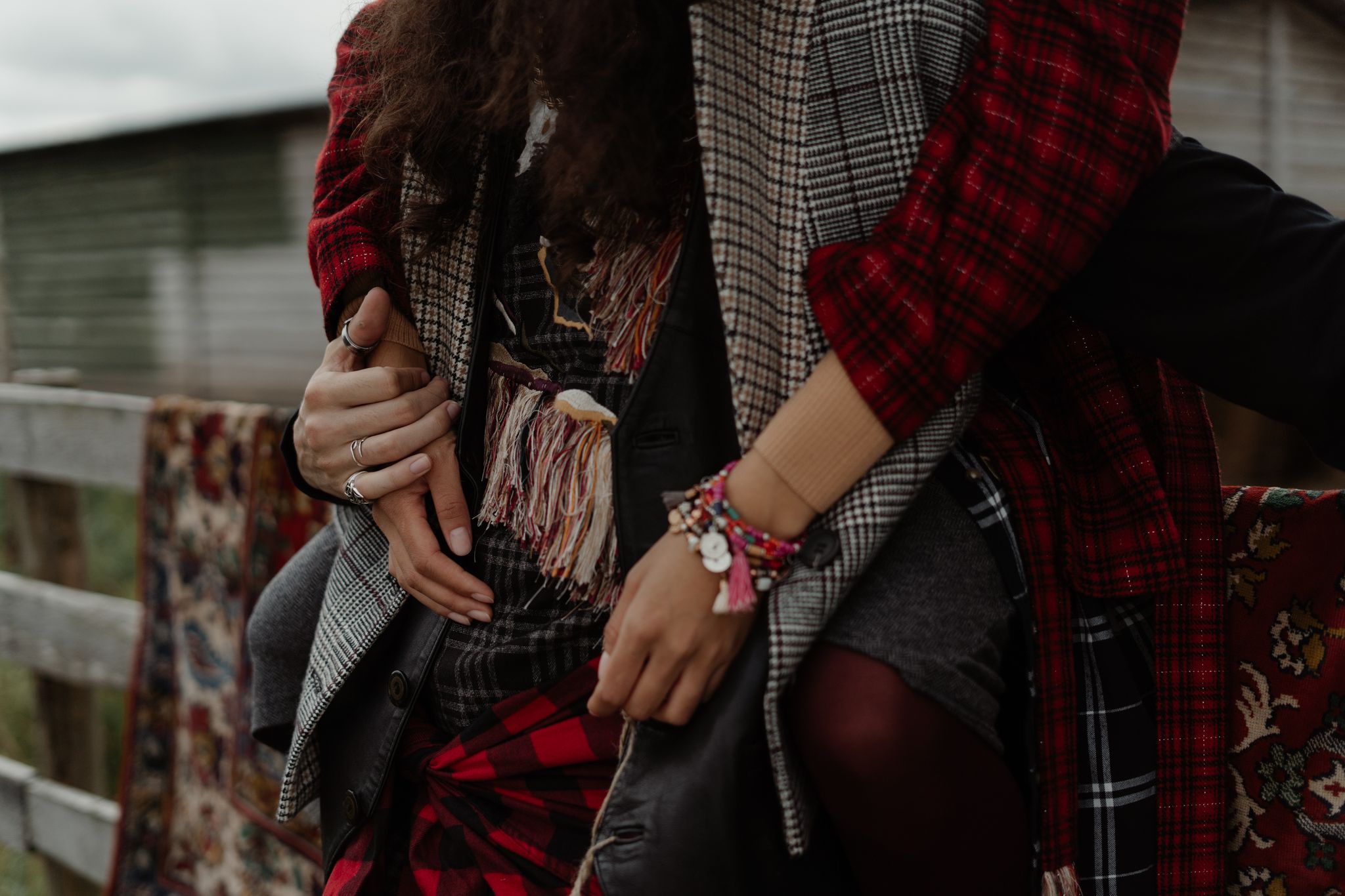 Close-up of a bohemian couple embracing in plaid and checked clothing by a wooden fence.