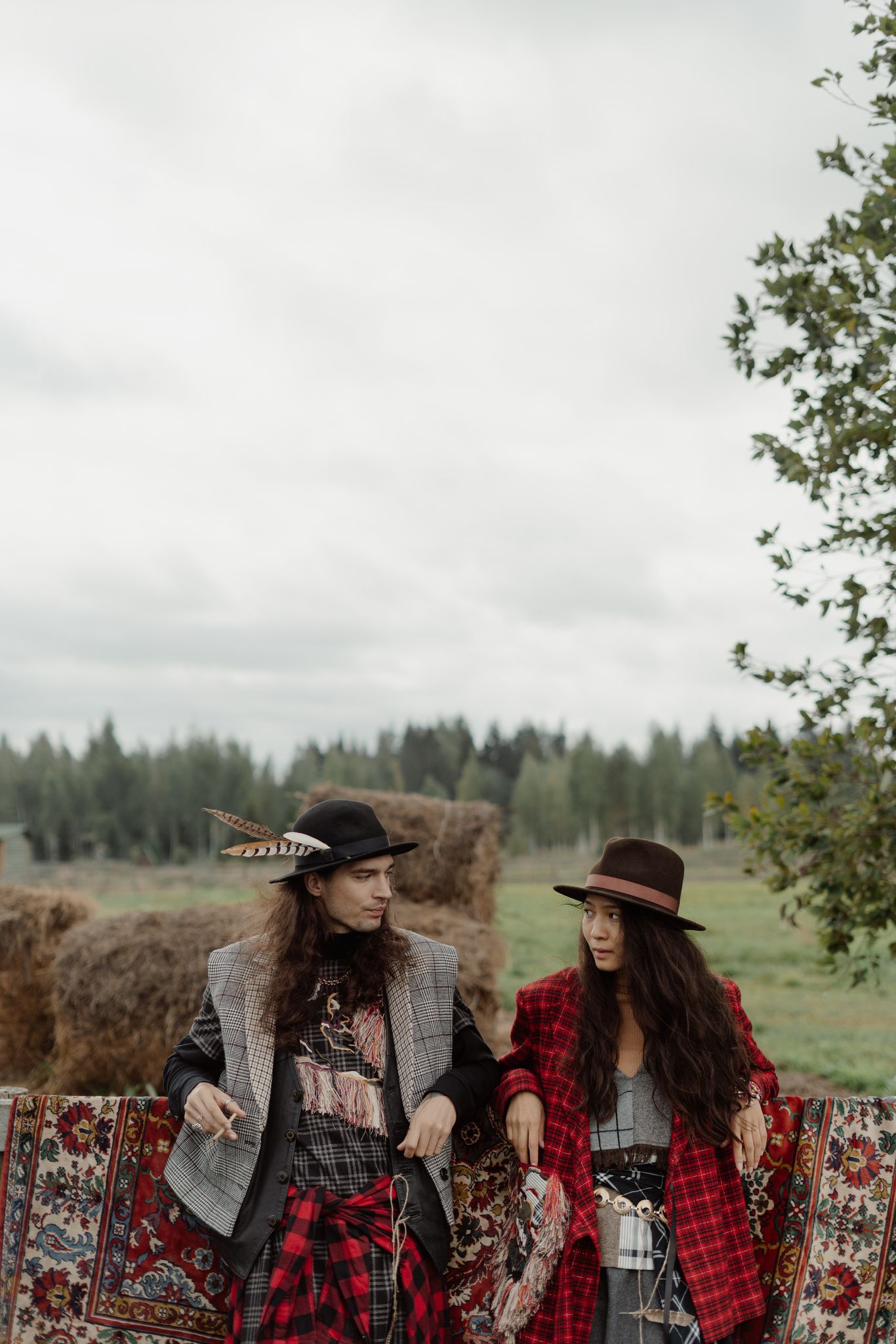Two people in bohemian attire posing on a hay field backdrop.